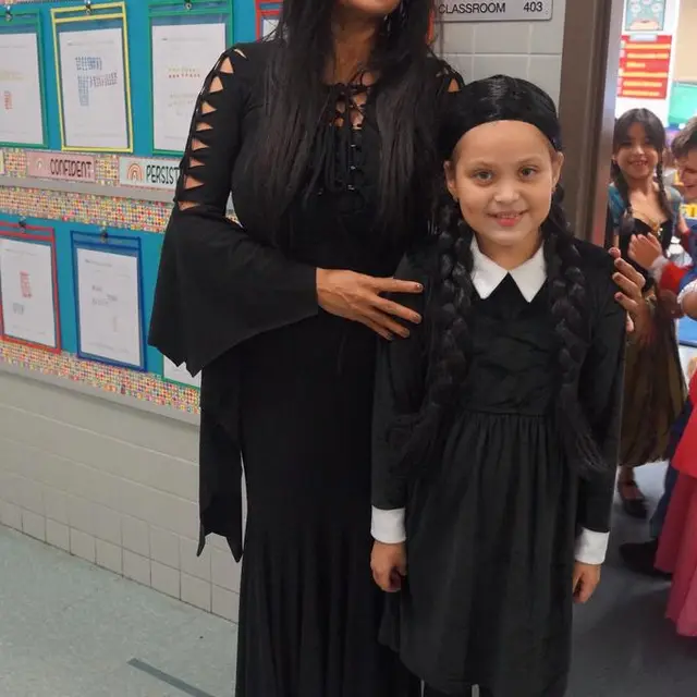 A staff member and a scholar dressed alike in black dresses with braided hair