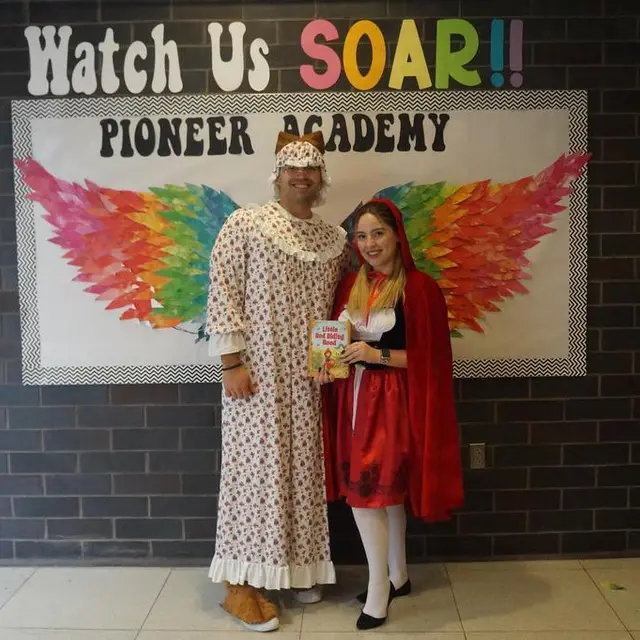 Two staff members dressed as Grandma and Little Red Riding Hood in front of the rainbow wings mural