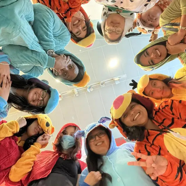 Scholars in animal onesies leaning into a circle, photographed from below