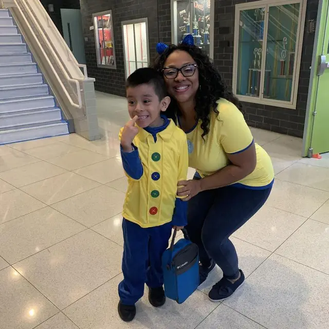 A staff member and a scholar in matching yellow and blue costumes in the hallway