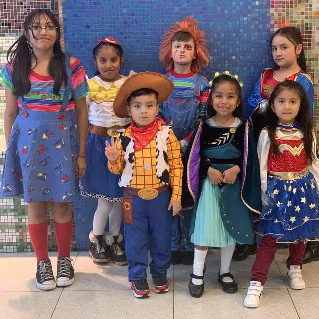 Scholars dressed as a cowboy, a doll and a superhero in front of the lobby mosaic