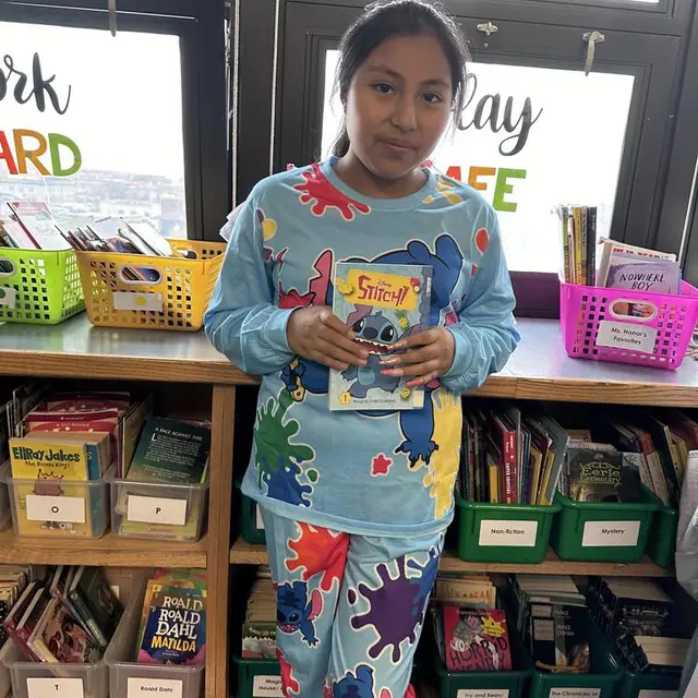 A scholar in a paint-splattered outfit holding a book in the classroom library