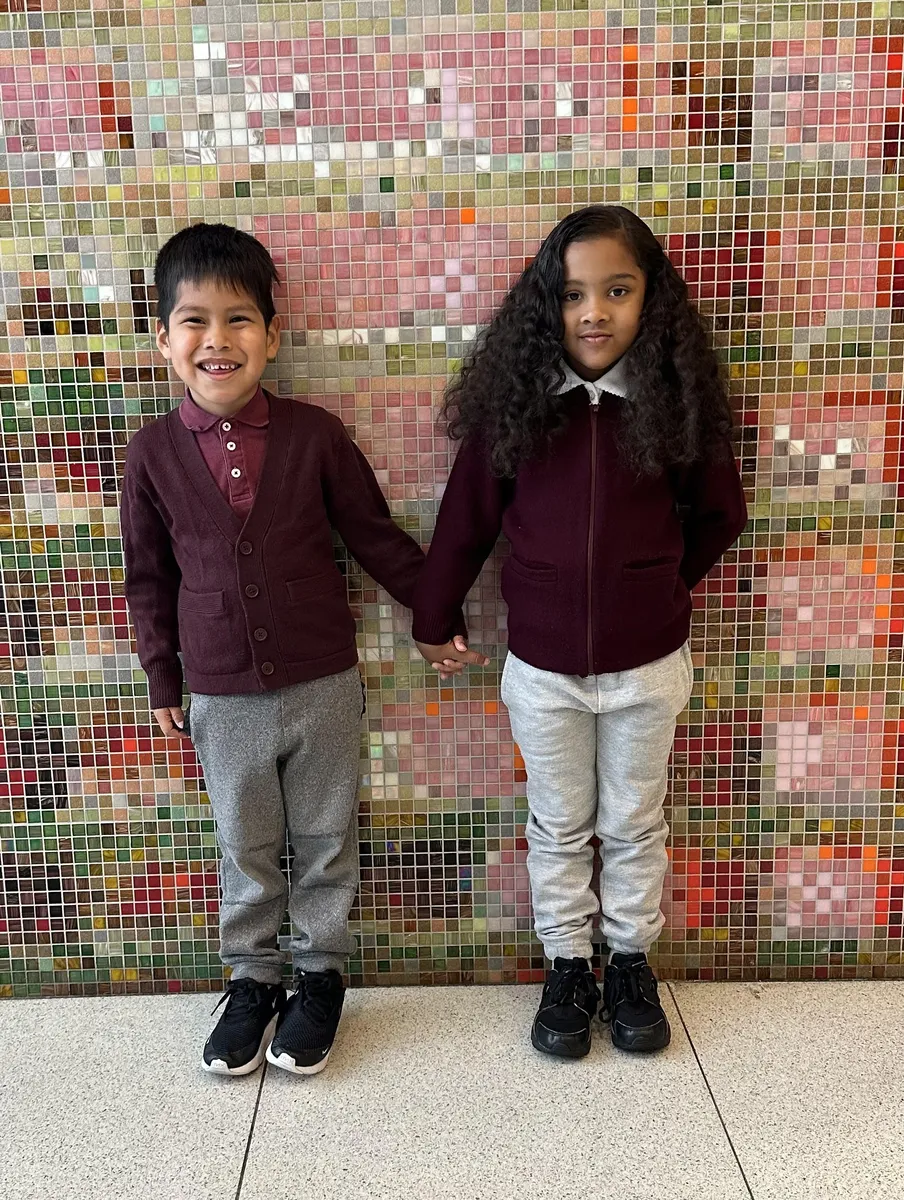 Two young scholars in front of the lobby mosaic wearing burgundy sweaters, gray sweatpants and black sneakers
