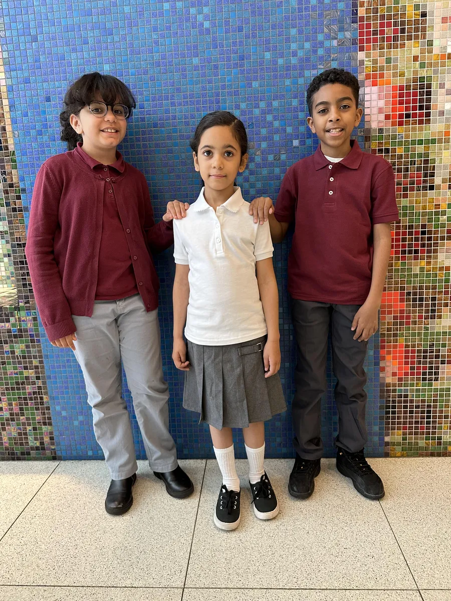 Three scholars in front of the blue lobby mosaic wearing burgundy and white polos, a burgundy sweater, gray pants and a gray skirt