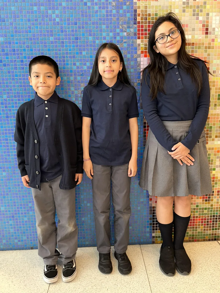 Three older scholars in front of the blue lobby mosaic wearing navy polos, a navy sweater, gray pants and a gray skirt